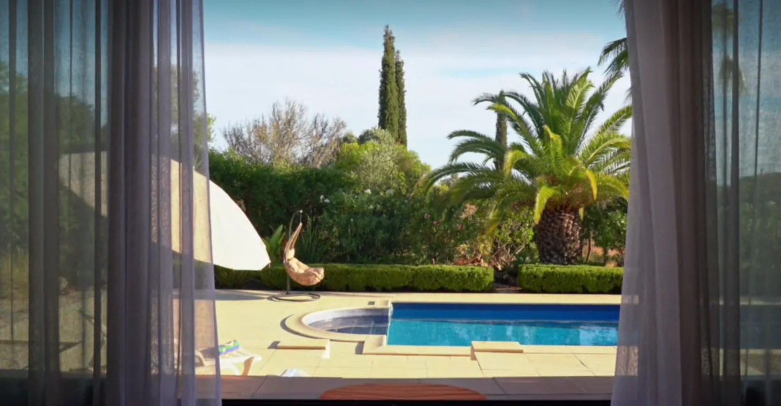 Blick durch Vorhänge auf einen Pool mit Palmen, das Bild der Startseite
